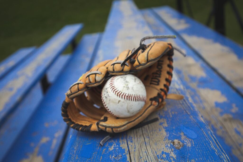 Close-up of a baseball and glove on a blue wooden bench, ready for play.